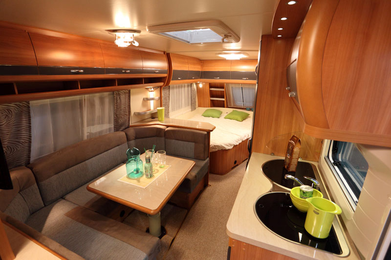 A gorgeous wood interior of a Class A motorhome with booth seating and a corner bed
