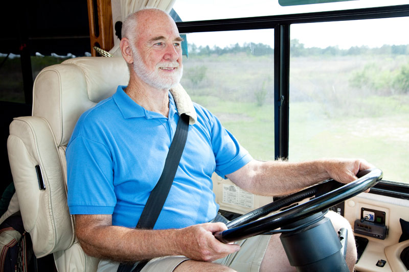 An older gentleman in the drivers seat of a Class A motorhome with his eyes on the road 